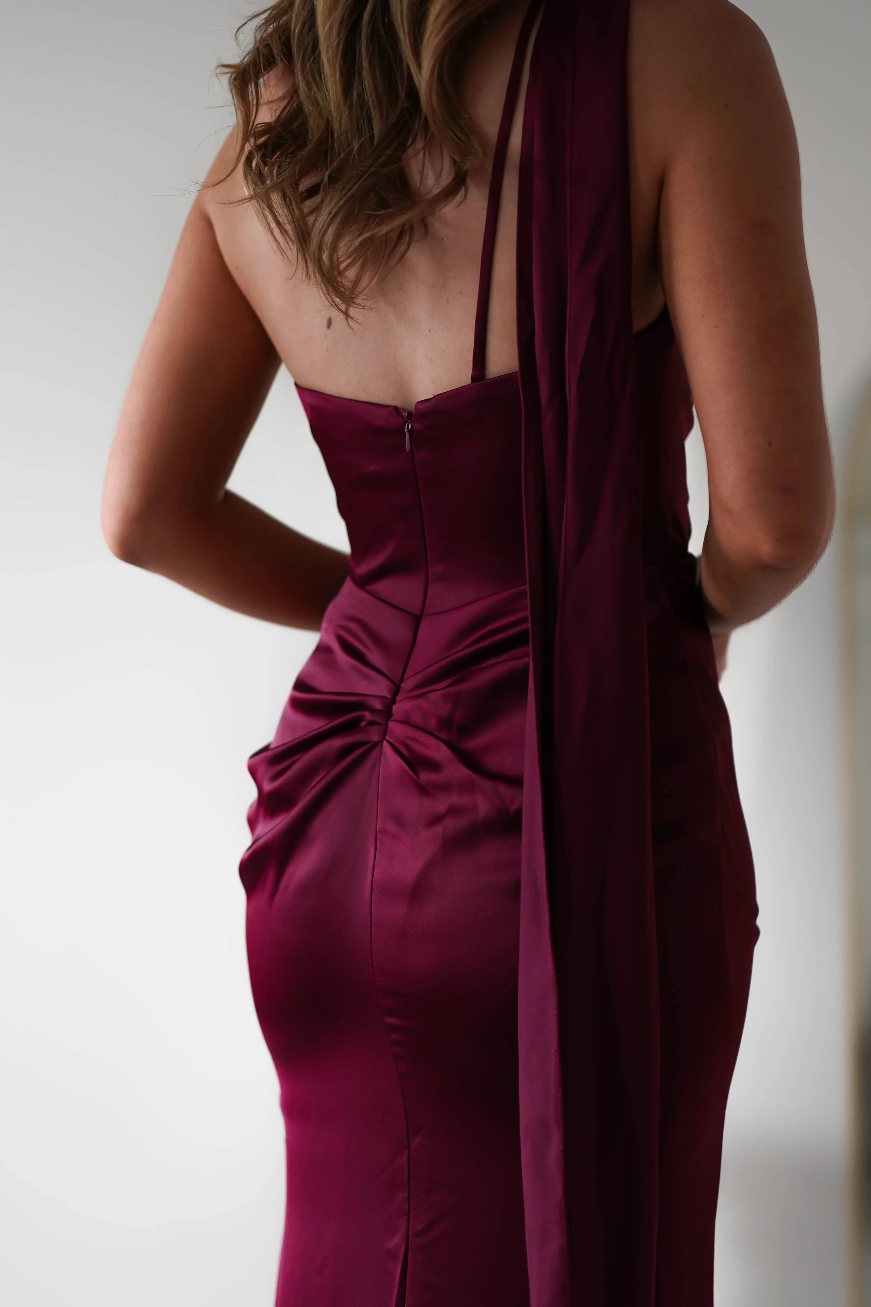 Robe Weitese en satin bordeaux, asymétrique, décolleté licou, corsage froncé en satin et fente haute spectaculaire.